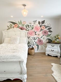 a white bed sitting in a bedroom next to a wall with flowers painted on it