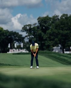 a man in yellow shirt and black pants on a green golf course with trees in the background