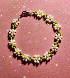 a bracelet made out of beads and flowers on a pink background with sparkles in the background