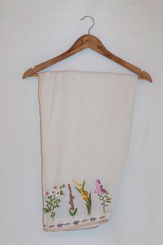 a white towel hanging on a wooden hanger with flowers and leaves embroidered on it