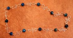 a necklace with blue beads and silver wire on a wooden surface, ready to be used as a bracelet