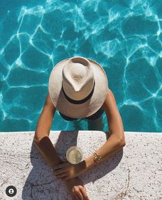 a woman sitting on the edge of a swimming pool with her hat over her head