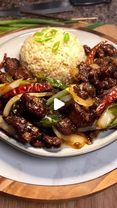 a white plate topped with meat and veggies next to rice on top of a wooden table