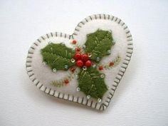 a heart shaped brooch with holly leaves and berries in the center on a white background