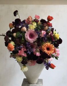 a white vase filled with lots of colorful flowers sitting on top of a stone block