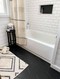 a bathroom with black and white tile flooring next to a bathtub, rug and window