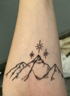 a tattoo on the arm of a person with mountains and stars in the sky above them