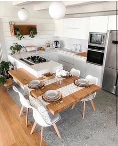 a modern kitchen with an island table and white chairs in the center, along with stainless steel appliances