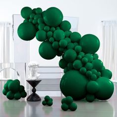 green balloons floating in the air next to a table with a vase and chair on it