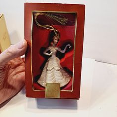 a hand holding an ornament in a red box with a white and black dress on it