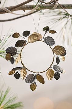 a circular metal decoration with leaves hanging from it's sides on a tree branch