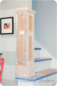 a tall cabinet sitting on top of a set of stairs next to a wall with pictures above it