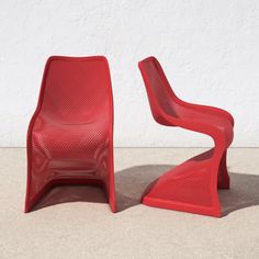 two red chairs sitting next to each other on top of a cement floor in front of a white wall