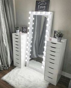 a white vanity mirror sitting on top of a wooden floor next to a dresser with drawers