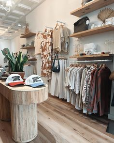 the inside of a clothing store with clothes on racks and hats hanging up in it