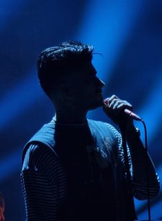 a man holding a microphone up to his mouth while standing in front of a blue light