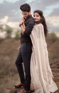 a man standing next to a woman on top of a dirt hill in front of a cloudy sky