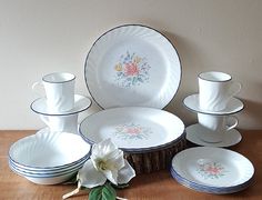 a table topped with lots of white plates and cups on top of a wooden table