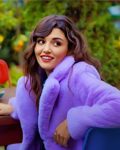 a woman sitting at a table wearing a purple coat