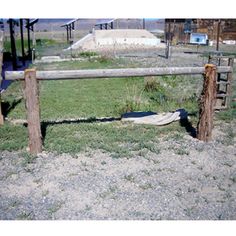 an old wooden fence in the middle of a field with grass and dirt on it