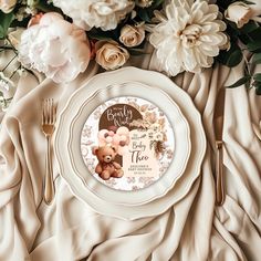 a white plate topped with a brown teddy bear on top of a table covered in flowers