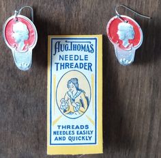 three pieces of jewelry sitting on top of a wooden table next to a packet of needle thread