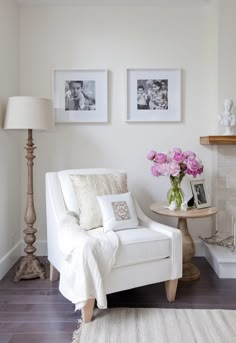 a white chair sitting next to a table with pink flowers on it and pictures above