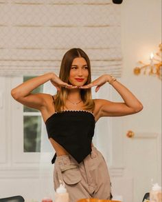 a woman standing in front of a table holding her hands up to her face and making the shape of a heart