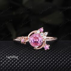 a pink ring with three stones on top and one stone in the middle, sitting on a black surface