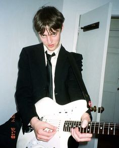 a young man in a suit playing an electric guitar