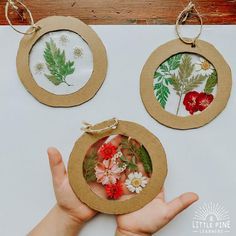 two handmade ornaments are being held in front of a white table with red and green flowers