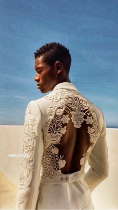 a man wearing a white suit with intricate lace on his back, standing in front of a blue sky