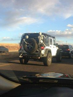 there is a jeep with a skeleton on it driving down the road in front of other cars