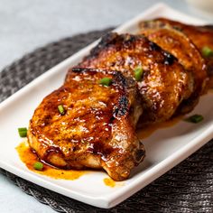 two pieces of meat on a plate with sauce and scallions next to it