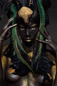 a woman in black and gold with feathers on her head, holding her hands to her face