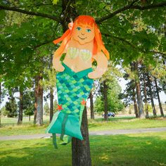 a paper cut out of a mermaid sitting on top of a tree in the park