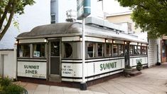 an old fashioned trolley car sitting on the side of a road next to a tall building