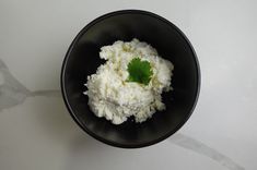 a black bowl filled with cottage cheese and garnished with a small green leaf