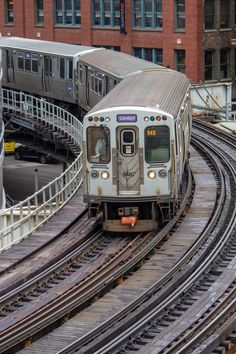 a silver train traveling down tracks next to tall buildings