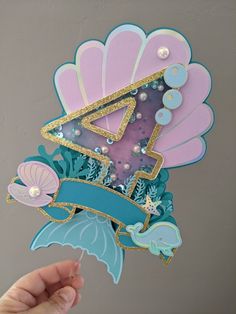 a hand holding up a card with an image of a mermaid tail and letter on it