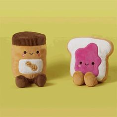 two stuffed animals sitting next to each other on a yellow background, one has a peanut butter and jelly sandwich