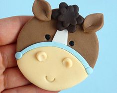 a hand holding a cookie shaped like a cow with a hat on it's head