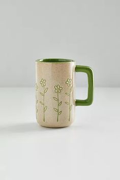 a green and white coffee mug with flowers painted on the side, sitting on a table