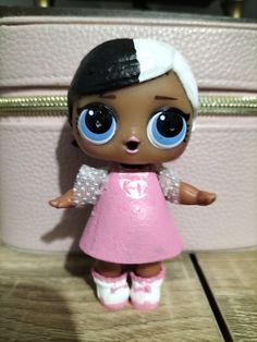 a little doll with big eyes standing next to a pink suitcase on a wooden floor