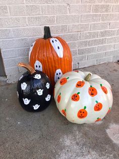 three pumpkins with faces painted on them sitting in front of a brick wall and door