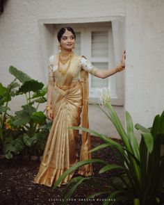 a woman in a gold and white sari posing for the camera with her hand on her hip