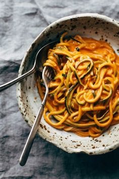 a white bowl filled with pasta and sauce on top of a gray table cloth next to a fork