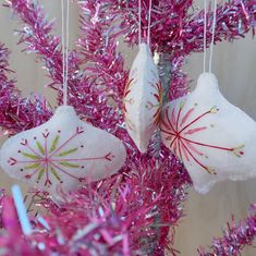 two white ornaments hanging from a pink tree with purple tinsel and red sprinkles