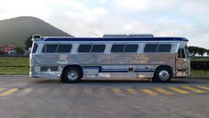 a silver and blue bus parked in a parking lot next to a mountain side area