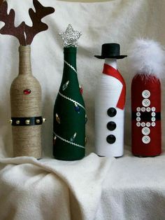 three wine bottles decorated with christmas decorations on a white cloth covered tablecloth, one has a snowman and the other is a reindeer